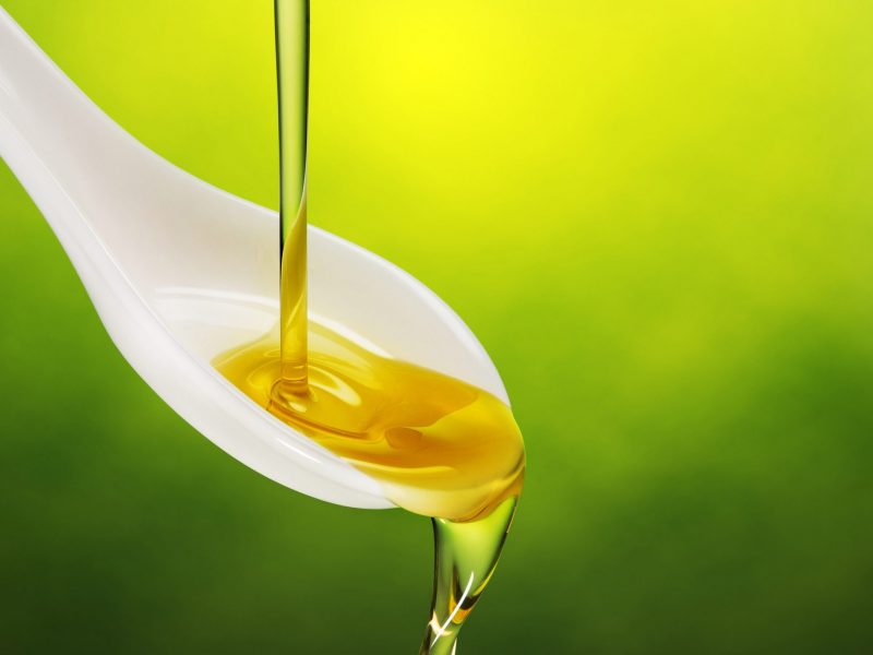 extra virgin olive oil poured in a spoon overflowing on green background